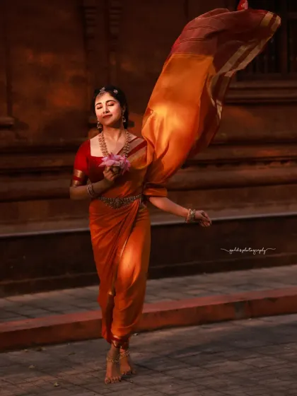 The movement of the saree in the wind adds a dynamic and ethereal element to this portrait. The bride holds a lotus, a symbol of purity and beauty.