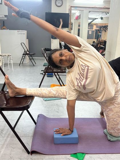 This student demonstrates a modified side stretch using a chair and block, showcasing how we adapt the practice to suit individual needs and flexibility levels.