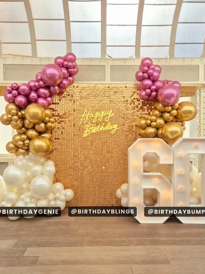 A sophisticated 60th birthday celebration with a gold shimmer wall and a balloon arrangement in magenta, gold, and white. The large, light-up '60' makes a bold statement.