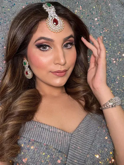 The client's hair is styled in soft, voluminous waves that complement her glamorous makeup and jewelry. This is a perfect look for a sangeet or cocktail party.