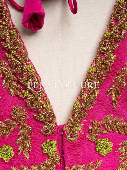 Grace in every detail. This pink net blouse features delicate leafy vines embroidered in gold and light green thread. The deep V-back and sheer sleeves add a touch of modern femininity.