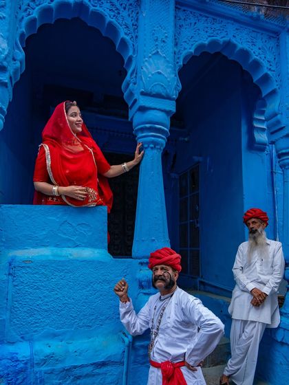 A lively scene in Jodhpur's blue city, with men in traditional attire and a woman in a red saree adding a splash of contrasting color. This frame is a perfect example of Rajasthani street life.