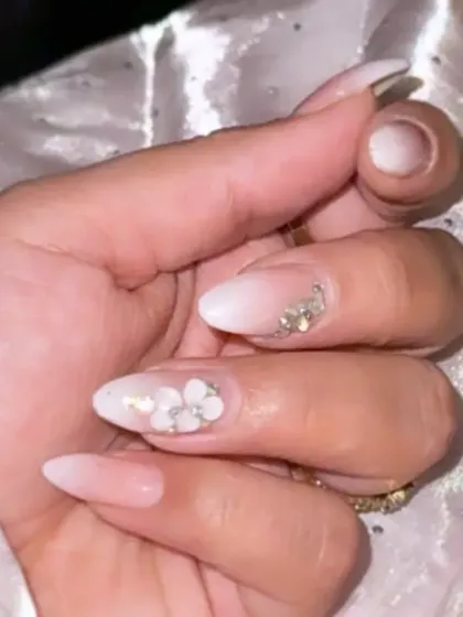 A soft white ombre manicure on almond nails, with a beautiful 3D white flower and crystal accent on the ring finger.