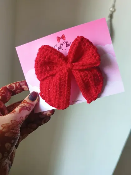 Holding up one of our vibrant red crochet Sailor Bows. The texture and craftsmanship make this simple bow a beautiful statement piece.