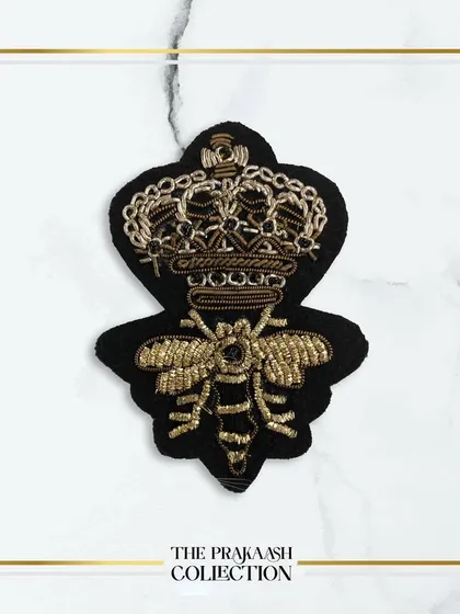 A detailed view of a hand-embroidered patch featuring a bee with a crown, crafted in gold thread on a black felt base. This is a popular motif for adding a touch of designer flair.