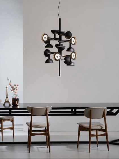 The Sibilla chandelier by Karman, with its intersecting arms and multi-directional lights, hangs over a dining table. This piece, inspired by Dutch neoformalism, acts as a complex geometric sculpture, diffusing light in all directions.