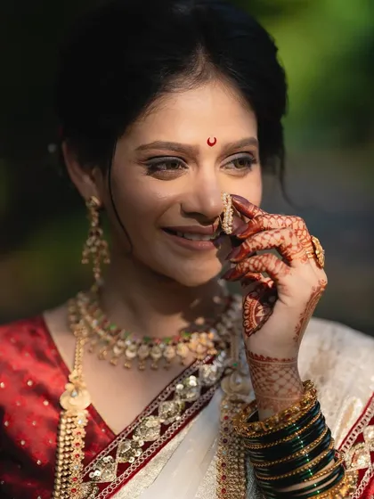 A close-up of the bride adjusting her nath. The soft smokey eye and the traditional chandrakor bindi create a look that is both bold and beautiful.