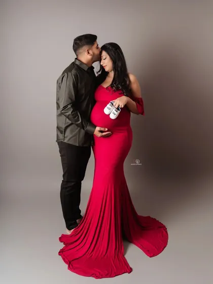 A classic pose that says it all. The vibrant red gown makes a beautiful statement, and the tiny shoes are a sweet hint of the little one on the way.