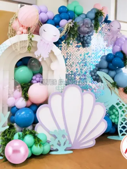 An elaborate 'Under the Sea' setup with a sequin backdrop, shell and coral cutouts, and a beautiful balloon arrangement creating an underwater feel.