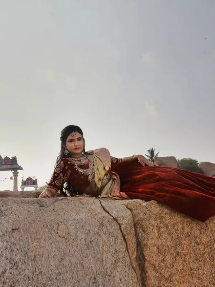 A relaxed, reclining pose that showcases the full traditional outfit. The composition uses the natural lines of the rocks to lead the eye towards the model.