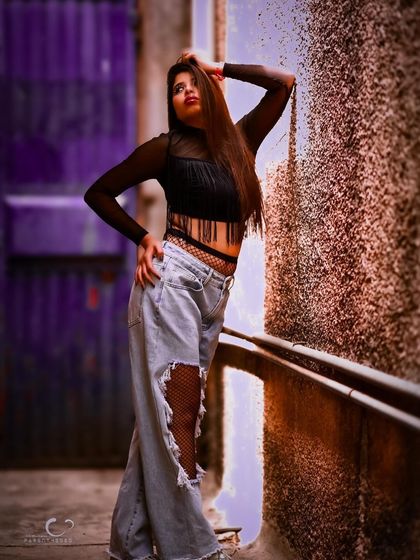 An edgy and cool outdoor shot in a purple-tinted alley. The ripped jeans and fishnets create a rebellious vibe that is full of attitude.