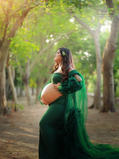 A powerful solo portrait of a mother-to-be with her bare bump, set against a beautiful natural backdrop. The green gown complements the lush surroundings.