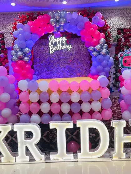 A full view of Kridha's Cocomelon birthday stage. The combination of a balloon arch, flower walls, a neon sign, and large marquee letters creates a truly grand and impressive setup.