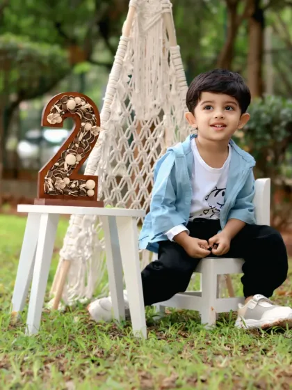 Celebrating turning two, this little boy sits proudly next to a '2' prop during his outdoor birthday session.