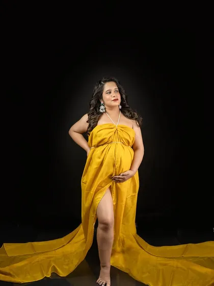 A powerful stance against a classic black backdrop. The vibrant yellow gown creates a stunning contrast, making this a truly eye-catching maternity portrait.