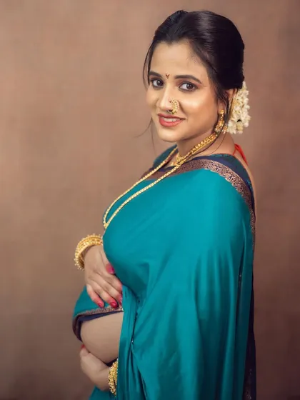 The beauty is in the details. This close-up portrait highlights the elegance of a traditional Maharashtrian look, from the classic nath and gold jewelry to the serene expression of the mother-to-be.