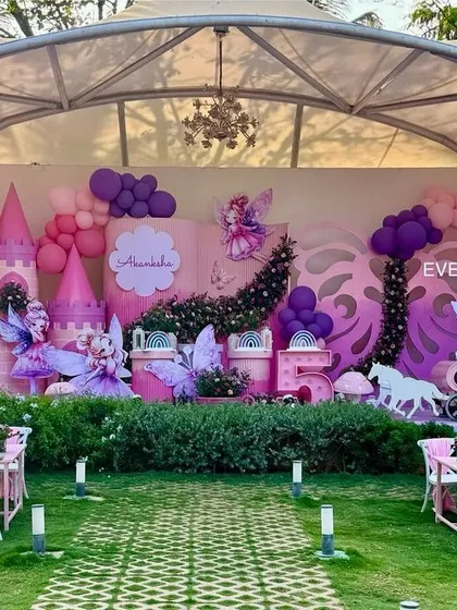 A sprawling outdoor venue transformed into an enchanted fairy land, with a custom-built castle, whimsical fairy cutouts, and themed tables for a magical garden party.