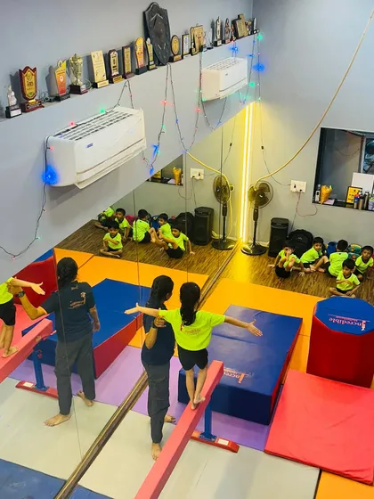 A bird's eye view of a typical gymnastics class at our Gorai studio. You can see children practicing on low balance beams with instructor assistance, while others wait their turn, showcasing our structured and supervised class environment.