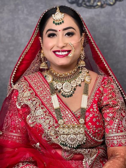 A stunning portrait of a bride in a red lehenga, with heavy, traditional Rajasthani jewellery. The makeup is bold and beautiful, with a focus on the eyes.
