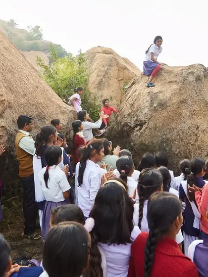 A group of schoolgirls watches one of their friends climb, cheering her on. This is what building a supportive community looks like from the very beginning.