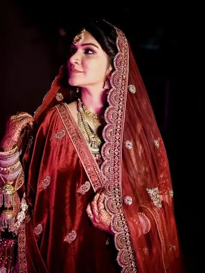 A close-up portrait that captures the bride's happy expression and the luxurious details of her red velvet dupatta. She radiates confidence and joy.