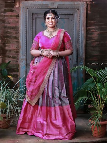 A full-length portrait showcasing a beautiful pink and grey half-saree. The bride's pose is graceful and elegant.