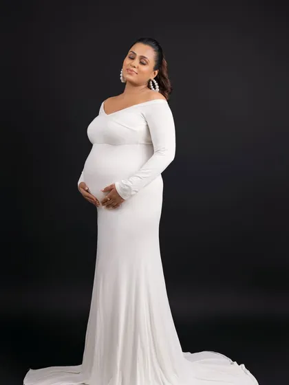A classic and elegant solo portrait in a simple white gown against a dramatic black background.