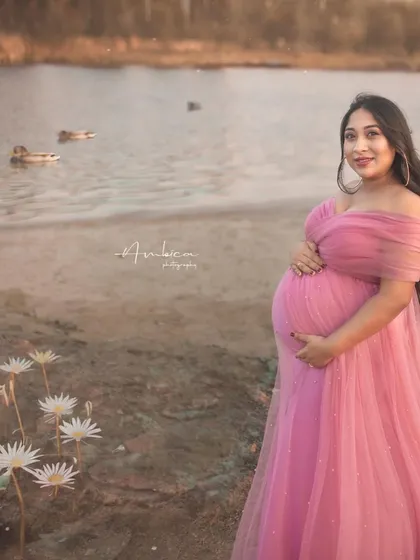 A serene portrait by the water. The combination of the pink gown, the calm lake, and the soft light creates a peaceful and picturesque maternity photo.