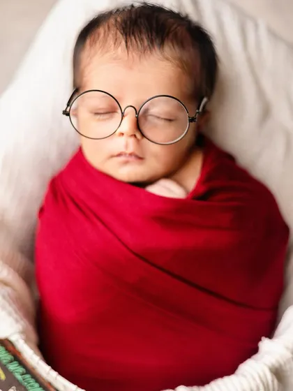 A close-up of a sleeping newborn, cleverly posed with round glasses for a "little professor" look.