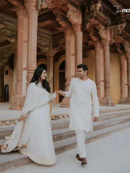 Walking hand-in-hand through the historic corridors of a Jaipur fort. The warm tones of the stone and the couple's serene white outfits create a beautiful, classic pre-wedding photograph that speaks of timeless love.