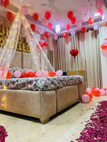 A soft and romantic first night setup using pink and red balloons with a delicate fairy light canopy and a path of rose petals.