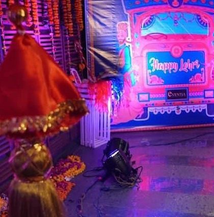 A vibrant, kitschy Lohri party setup. The backdrop with a colourful truck and dhol players sets a fun, Punjabi theme for a night of bonfire, music, and celebration.