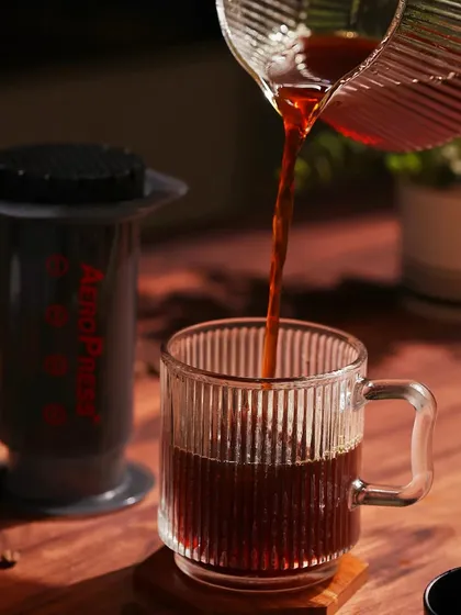 A shot of coffee being poured from an Aeropress. The warm lighting and wooden elements create a cozy, rustic feel.