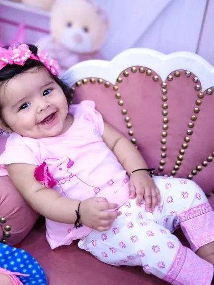 A beautiful, dimpled smile from a baby girl sitting on a pink shell-shaped couch.