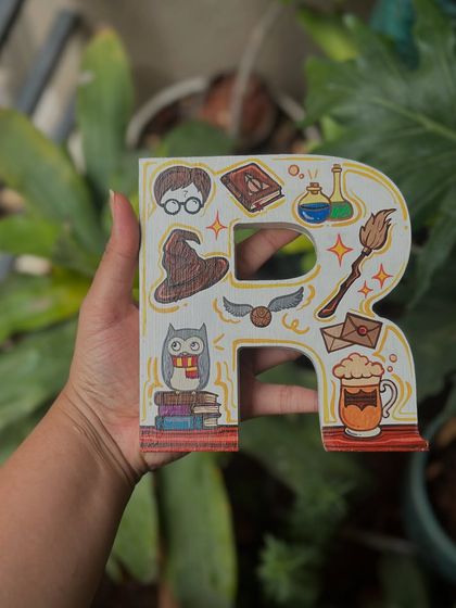 A Harry Potter-themed wooden letter 'R', decorated with iconic symbols from the series like the sorting hat, golden snitch, and a mug of butterbeer.