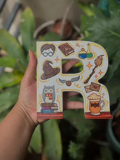 A Harry Potter-themed wooden letter 'R', decorated with iconic symbols from the series like the sorting hat, golden snitch, and a mug of butterbeer.