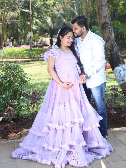 A tender moment between a couple in a sunlit park. The layered lavender ball gown adds a touch of soft romance to this beautiful outdoor maternity photo.