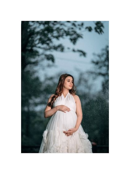 An outdoor portrait of a mom-to-be in a beautiful white gown, looking thoughtfully into the distance. The natural, slightly moody lighting adds a touch of drama to the scene.