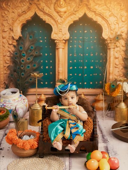A beautiful portrait of a baby as Krishna, with a serene expression, set against a backdrop with peacock motifs and traditional decor.