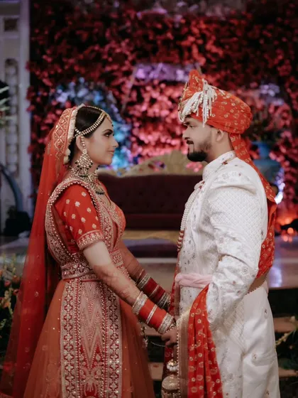 A classic portrait of Vaishali and her groom, their gazes locked, standing before a wall of red flowers.
