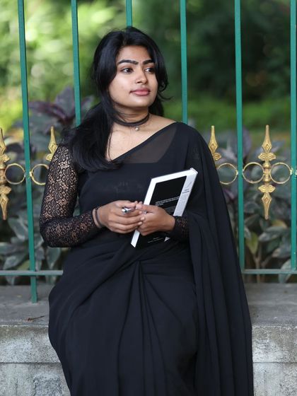 A full-shot from a professional photoshoot in a classic black saree. The makeup is clean and defined, with a focus on sharp brows and a neutral lip to suit the elegant theme.