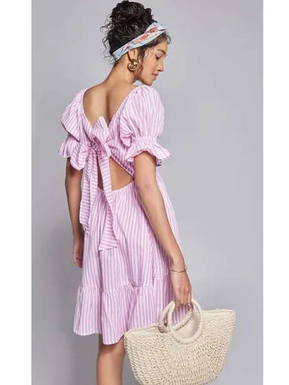 This image from a summer campaign features a pink and white striped dress with a cute back-tie detail, paired with a straw bag for the perfect vacation look.