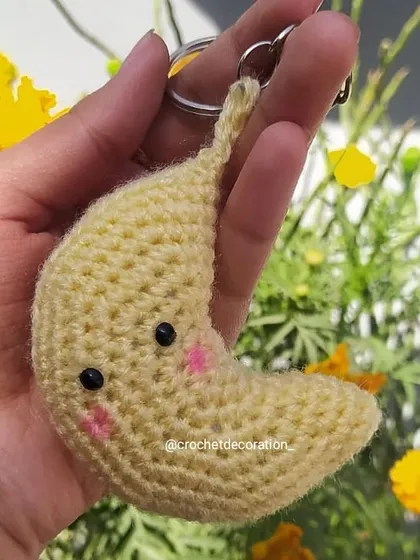 A cute and cuddly crochet moon keychain with rosy cheeks. This adorable accessory is perfect for personalizing your keys or bag and is crafted from soft, pale yellow yarn.