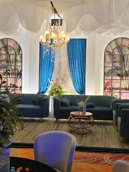 A comfortable lounge area with deep teal sofas set against a backdrop of stained-glass style windows and elegant blue drapes.