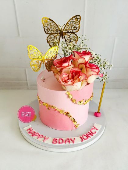 An elegant pink cake with a gold fault line design, topped with fresh roses and golden butterflies.