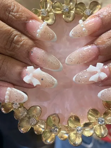 A soft and delicate French manicure with a glitter ombre effect, adorned with tiny pearls and 3D white bows.