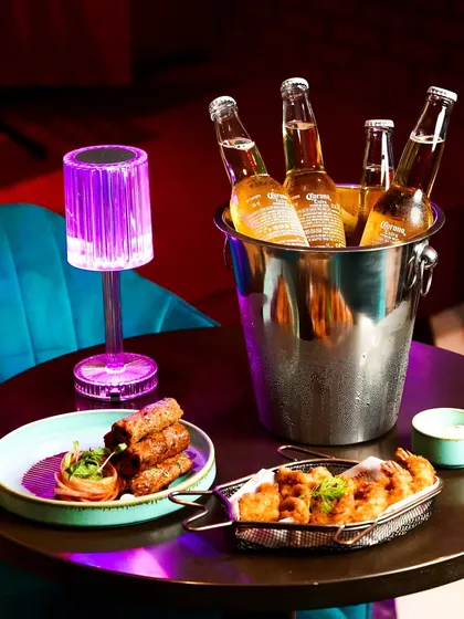 A bucket of ice-cold beers served with bar snacks in a lounge with purple mood lighting. This shot perfectly captures the atmosphere of a fun night out.