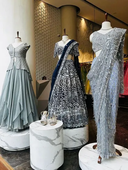 A display of our cool-toned evening wear. A navy blue lehenga with intricate silver embroidery is flanked by a grey peplum gown and a shimmering silver saree.