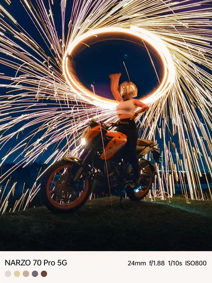 A steel wool photography tutorial using the realme Narzo 70 Pro. This shot shows a model on a bike surrounded by a circle of fire.