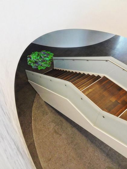 A view from above shows how a staircase can become a sculptural element within a larger space. The clean white lines of the balustrade contrast with the dark, curving floor plates, creating a dynamic composition.